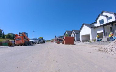 Parker, Colorado, ABD-Haziran 18, 2025 - Birçok turuncu inşaat kamyonu ve kırmızı bir çöp konteynırı banliyödeki evlerin önünde park edilmiş durumda. Görüntü açık ve minimal ışıklandırma gösteriyor