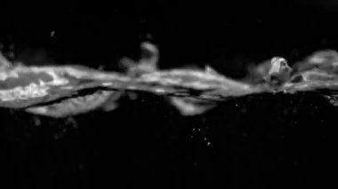 Kabarcık dalgaları sol alttan yavaşça patlıyor ve siyah bir arkaplanda suya yayılıyor..