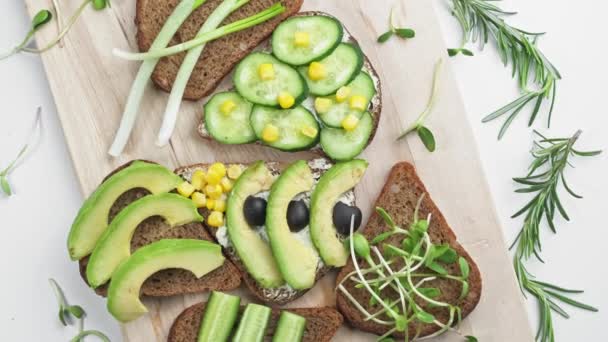 Sandwich met avocado, komkommer, olijven en groene uien op een houten plank. — Stockvideo