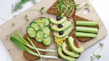 Avokado, humus, salatalık, ayçiçeği filizli sağlıklı sandviçler. Tahta bir kesme tahtasının üzerinde, üst manzara. Sağlıklı Vejetaryen Atıştırması