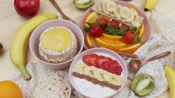 Sabah kahvaltısı meyveli, yoğurt muzlu ve çilekli bal cipsi dilimlenmiş portakallı sağlıklı kahvaltı konsepti. Üst görünüm — Stok video