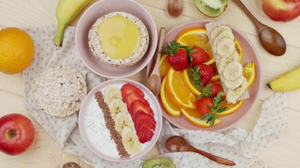 Lekker ontbijt. Granola met aardbeien en banaan en vers gehakte sinaasappelpartjes, gegarneerd met diverse vruchten, zoet ontbijt — Stockvideo