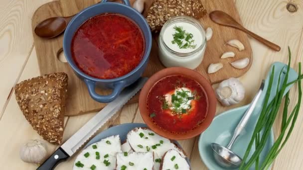 Cozinha russa e ucraniana. Borscht com creme azedo e especiarias, ervas frescas, alho e pampushki. Sopa de beterraba em uma tigela azul em uma tábua de madeira. Vista superior — Vídeo de Stock