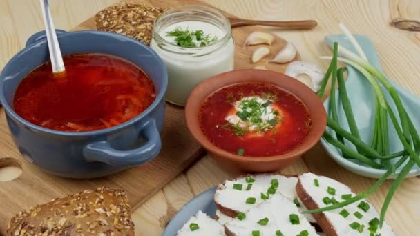 Russian and Ukrainian cuisine. Borscht with sour cream and spices, fresh herbs, garlic and pampushki. Beetroot soup in a blue bowl on a wooden board. — Stock Video