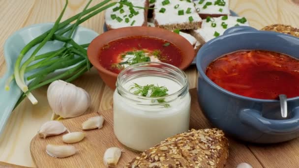 Cozinha russa e ucraniana. Borscht com creme azedo e especiarias, ervas frescas, alho e pampushki. Sopa de beterraba em uma tigela azul em uma tábua de madeira. — Vídeo de Stock