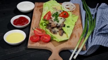 Mantarlı ve peynirli vejetaryen yeşil pita ekmeği ahşap bir masada döner. Domateslerin, yeşilliklerin ve çeşitli sosların etrafında.