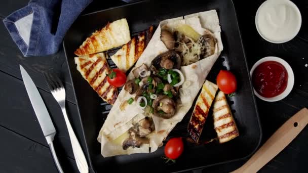 Вегетарианский пита-хлеб с грибами и сыром вращается на деревянном столе в квадратном сковороде с жареным сыром и помидорами. Разные соусы вокруг. Чёрный фон — стоковое видео