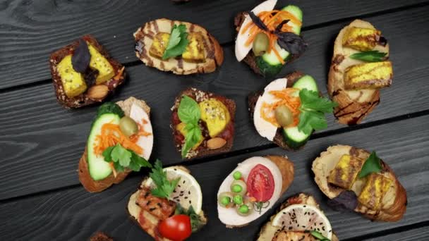 Deliciosos petiscos. Lanches Bruschetta. Variedade de pequenos sanduíches com verduras - tomate, arugula, pimentão. vista de cima. vista superior. fundo de madeira preta — Vídeo de Stock