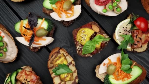 Delicious snacks. Bruschetta snacks. Variety of small sandwiches with vegetables - tomato, arugula, pepper. view from above. top view. black wood background — Stock Video