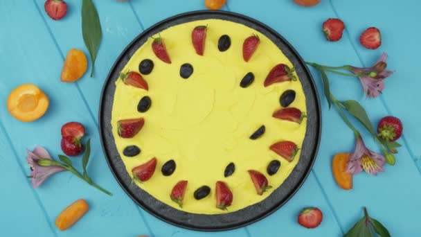 Napfényes sárga torta. A sodó világos színű. Friss bogyókkal díszítve. Eper, áfonya és még több. kék háttér. Lapos fektetés — Stock videók