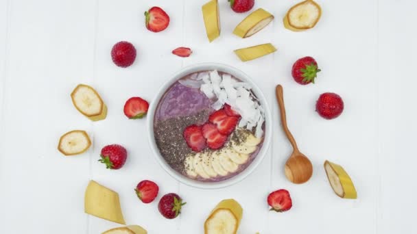 Een kom vegetarisch ontbijt met aardbeien, yoghurt en chiazaad van een witte houten tafel. Gezond voedselconcept — Stockvideo