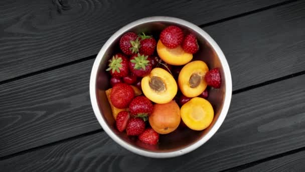 Apricot strawberries washed bowls on black wooden background. rotating background — Stock Video