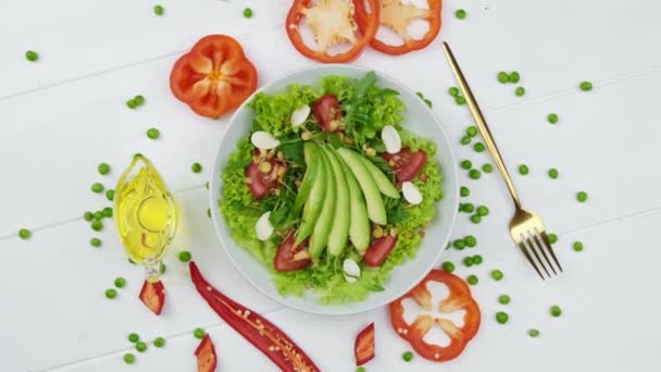 Lechuga hojas de tomate de aguacate concierto de comida saludable ensalada adornada con trozos de pimiento rojo y aceite para cubrir — Vídeo de stock