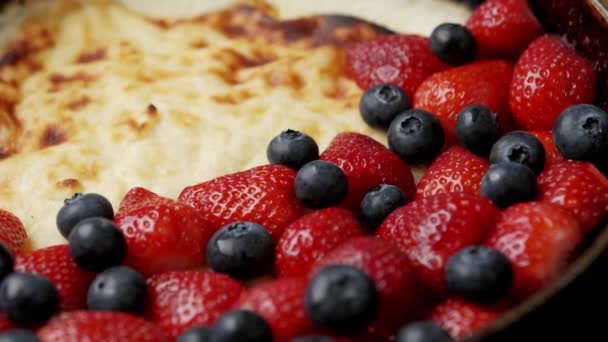 Pastel de cuajada frito en una sartén con fresas y arándanos en una mesa de madera. De cerca. — Vídeo de stock