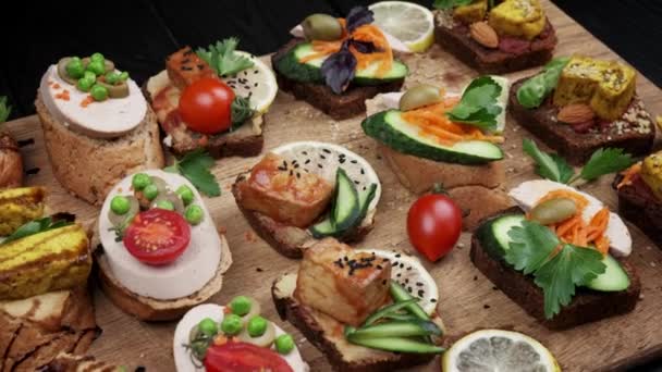 Délicieuses collations. Des snacks à la brosse. Variété de petits sandwichs aux légumes - tomate, roquette, poivre. vue d'en haut. vue de dessus. fond en bois noir — Video