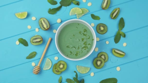Zoet dessert met spirulina op een blauwe houten achtergrond. met schijfjes kiwi, limoen bestrooid met muntblaadjes — Stockvideo