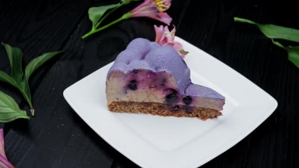 Slice of cheesecake with blueberry and black currant on white plate over wooden background — 图库视频影像