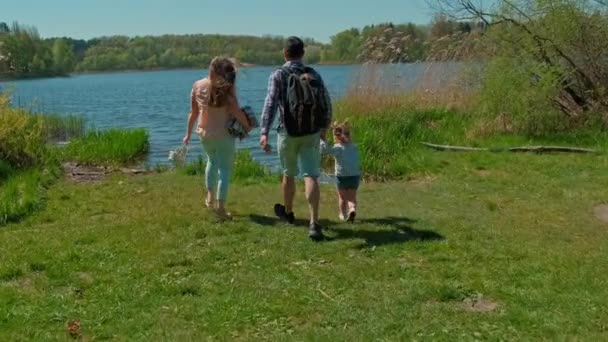 Happy cute family walking in nature park by lake. Parents with child walking. Family picnic by lake. Hiking in natural park Vidéo De Stock Libre De Droits