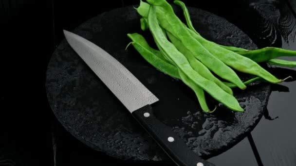 Frijoles verdes recién cortados y un cuchillo sobre una mesa rústica de madera negra. — Vídeos de Stock