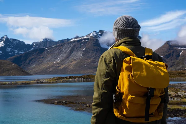 En fyr reiser med gul ryggsekk gjennom pittoreske steder med vakre fjellandskap. – stockfoto