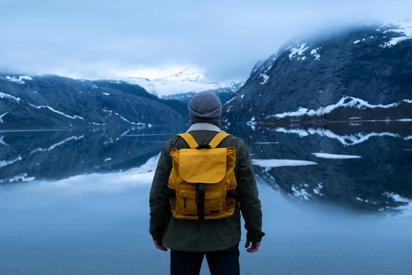 En fyr reiser med gul ryggsekk gjennom pittoreske steder med vakre fjellandskap. – stockfoto
