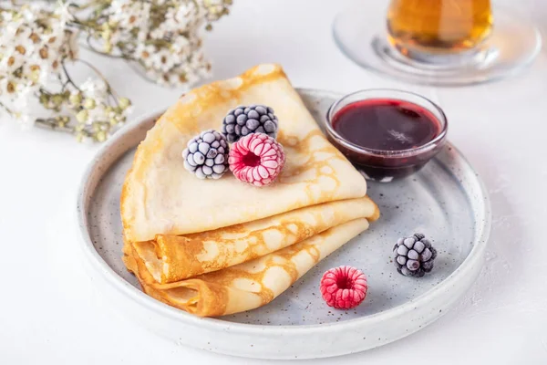 Crepes with berries and red sauce on a plate. Thin pancakes with ice  fresh berries.