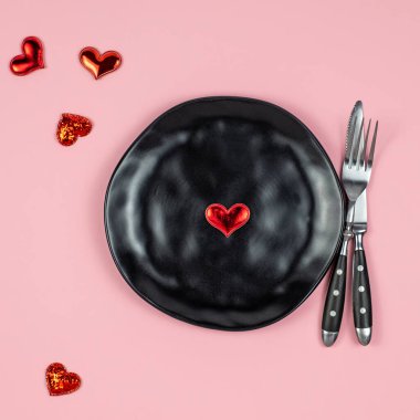 Çatal, bıçak, tabak ve kalplerle donatılmış pembe arka plan. 