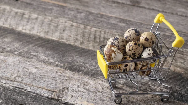 Quail eggs in a small shop trolley on a wooden background.. Rustic style. Space for text