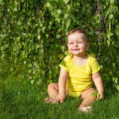 Küçük çocuk yeşil çimenlerde oturuyor ve gülümsüyor.