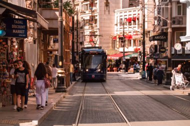 İSTANBUL, TURKEY - 09 07 2020: İstanbul 'un tarihi Hocapasa ilçesinde Hudavendigar caddesi boyunca gün batımı manzarası, Türkiye' de dar kaldırımlarda yürüyen turistler ve kaldırımlı bir tramvay