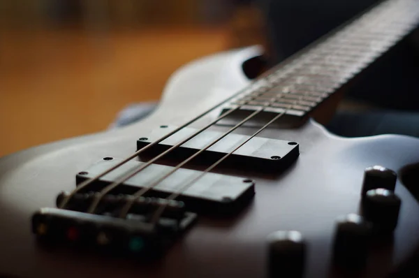 Pürüzsüz bir vücudun yakın çekimi, pikaplar, köprü, düğmeler ve arka fonda müzik aleti olan bas gitar telleri.