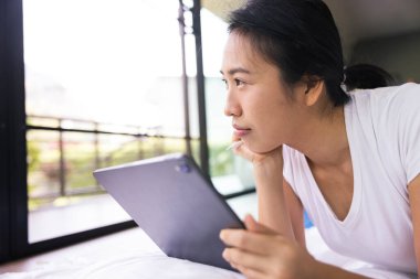 Evdeki yatakta dijital tablet kullanan bir kadın. Yeni nesil, aile, ebeveynlik, gerçeklik, bağlantı, teknoloji kavramının kullanımı.