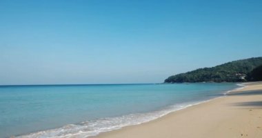 Mavi gökyüzüne karşı mavi denizi olan yumuşak bir sahil. Naithon Sahili, Phuket, Tayland 'da kıyıya vuran beyaz dalgalarla. Doğa, seyahat, gerçek, özgürlük kavramları. video 4K.