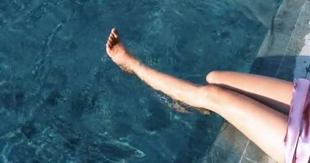 夏には 太陽の下でリゾートプール内の青い水に対して細い足のクローズアップ 女は足をプールの水にぶら下げている コンセプトの画像については リラックス リゾート — ストック動画