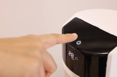 Yakın plan Asyalı kadın eli, yatak odasındaki hava temizleme makinesinin düğmesine basıyor. Başbakan 2.5. Toz ve hava kirliliği kavramını koruyun. Hava temizleyici evdeki ince tozu temizliyor..