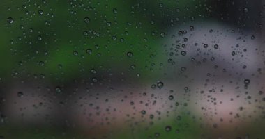 Bulanık şehir trafik geçmişine sahip araba camına yağmur damlalarının soyut deseni. Yağmurlu gün havası ve üzgün ruh hali konsepti. Yüksek kalite 4K video.