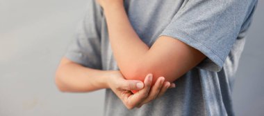 Kadın eli kırmızı iltihaplı yaralı dirseğini tutuyor. Eklem ağrısı, kas hasarı, eklem iltihabı, tendonit, spordan dolayı ağrı ya da arka planda çalışma kavramı.