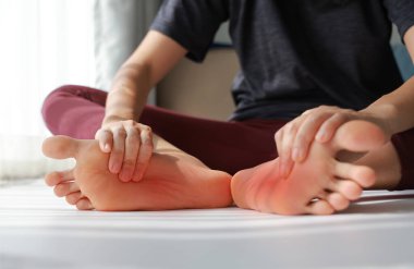 Kadın oturuyor ve her iki ağrılı ayağına da tabanı kırmızı renklerle masaj yapıyor. Ayak ağrısı, plantar fasiiti, aşırı kullanılmış ayak ve çevresel nöropati konsepti sağlık ve terapi için..