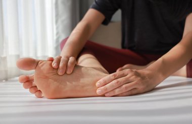 Kadın oturuyor ve her iki ağrılı ayağına da tabanı kırmızı renklerle masaj yapıyor. Ayak ağrısı, plantar fasiiti, aşırı kullanılmış ayak ve çevresel nöropati konsepti sağlık ve terapi için..