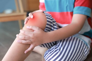 Küçük çocuk dizinde iltihaplı kırmızı bir diz tutuyor. Elleri eklem ağrısı çekiyor ya da evinde kazara yaralanmış. Pediatrik sağlık hizmeti kavramı, çocuklarda kemik sorunları ve ortopedik tıbbi tedavi.