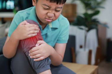 Asyalı çocuk eklem yaralanması ya da kazadan dolayı dizinde iltihaplanma olan acı dolu bir yüz ifadesi gösteriyor. Çocukluk kemik sorunları, büyüme ağrısı ve ortopedik tedavi konsepti.
