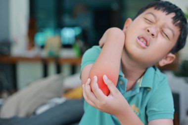 Dirsek ağrısı çeken Asyalı bir çocuk. Ağrılı bölgede kırmızı röfle, kol kası yaralanması, eklem iltihabı, kazara kemik kırığı ya da evde deri tahrişi sorunu var..