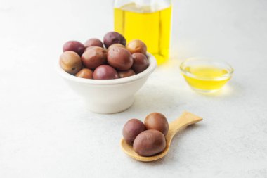 Kalamata zeytinleri beyaz kasede, arka planda yağ şişesi var.