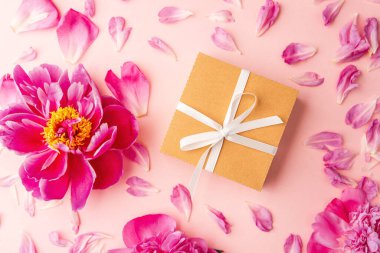 Beyaz kurdeleli hediye kutusu ve pastel arka planda pembe şakayık çiçekleri dağınık taç yapraklarıyla