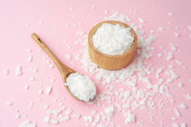 Ahşap kase ve kaşık, pastel pembe arka planda soya yağı taneleri.