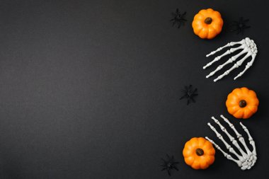 Turuncu balkabakları, siyah örümcekler ve siyah yüzeye dizilmiş beyaz iskelet eller.