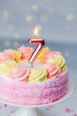 Renkli kremayla süslenmiş pembe bir pasta bir çocuğun yedinci yaş gününü kutlar..