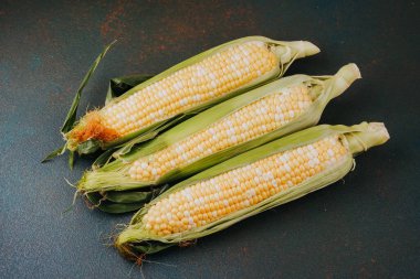 Mevsimlik tarım hasadı ya da sağlıklı yemek malzemesi fotoğrafçılığı için kabuklu üç taze mısır koçanı.