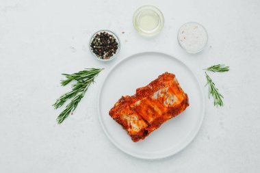 Beyaz tabakta marine edilmiş domuz pirzolası, biberiye ve baharatlı.