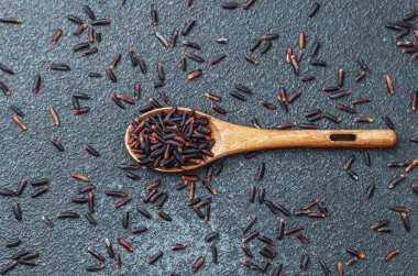 Koyu arka planda siyah pirinçli ahşap kaşık ve dağınık taneler.